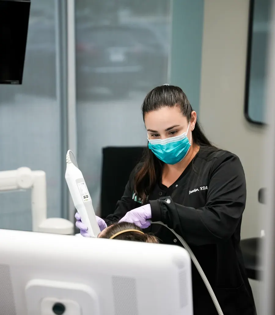 A Montz & Maher team member in a mask scanning a patient's teeth with an intraoral scanner.